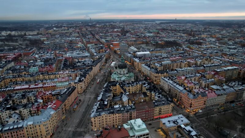 Aerial view of Stockholm, Sweden, showcasing the city's historic architecture, colorful buildings, and streets bustling with activity as the day transitions to evening under a cloudy sky