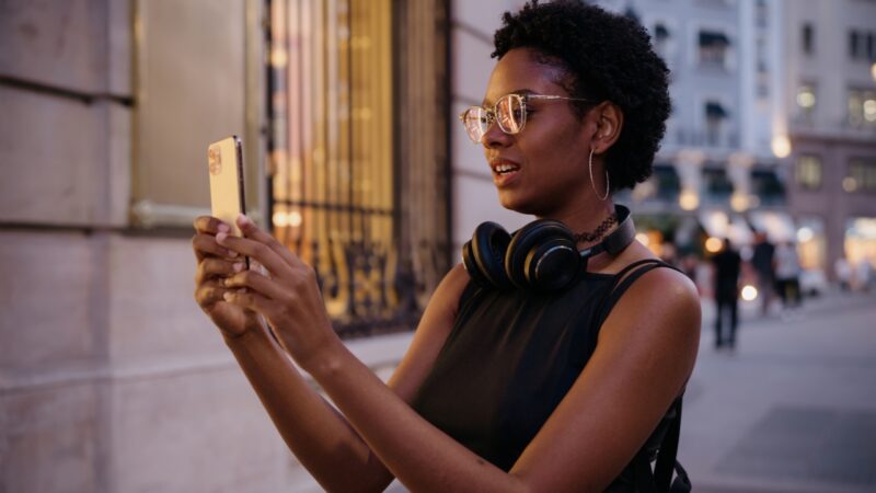 A woman uses her phone on a city street with headphones around her neck
