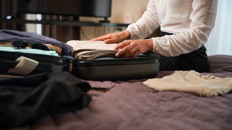 A person packs folded clothes into a suitcase on a bed